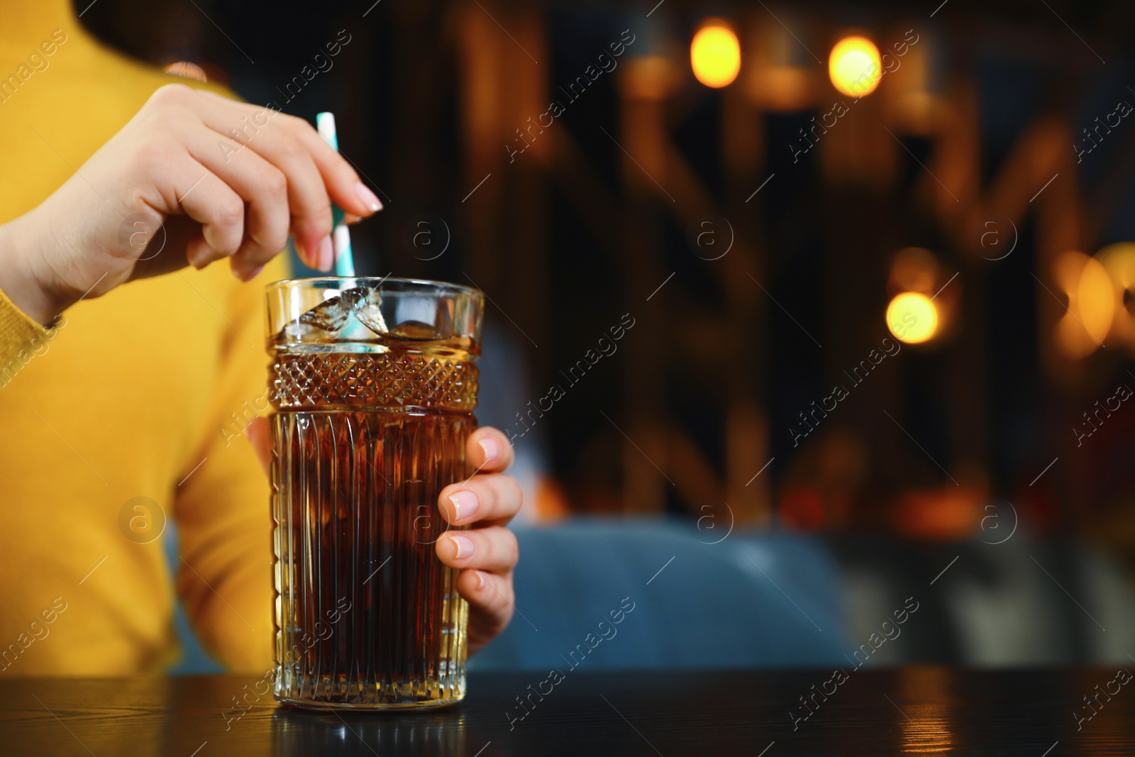 Photo of Woman with glass of refreshing cola at table indoors, closeup. Space for text