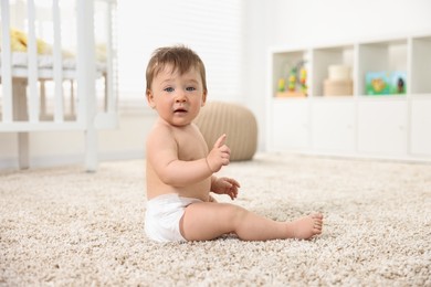 Cute baby boy sitting on carpet at home