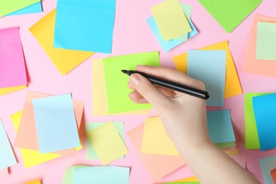 Photo of Woman writing on sticky note against pink background, top view