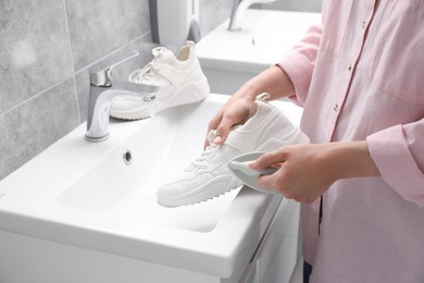 Photo of Woman washing stylish sneakers with brush in sink, closeup