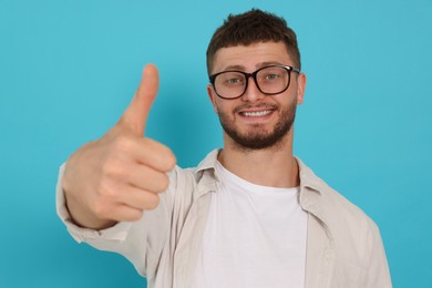 Young man showing thumb up on light blue background