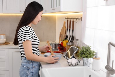 Photo of Woman looking at recipe on tablet while cooking in kitchen