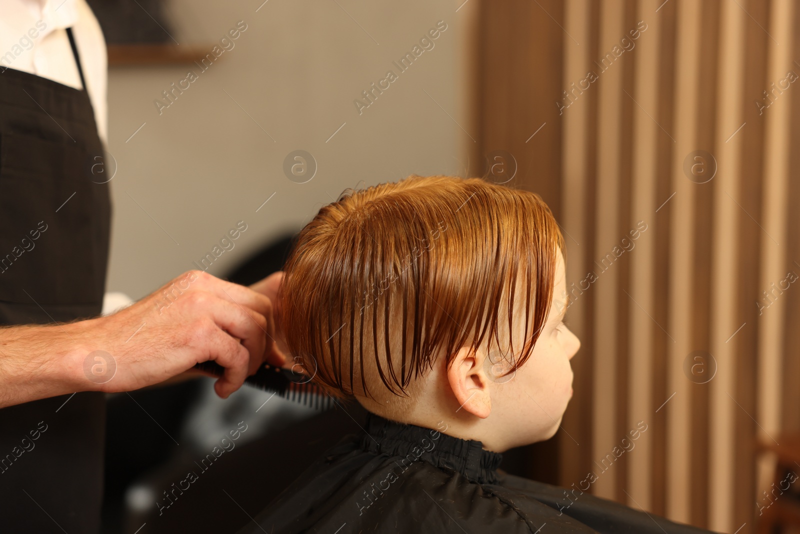 Photo of Professional hairdresser combing boy's hair in beauty salon, closeup