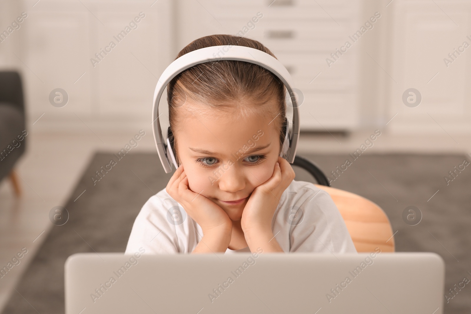 Photo of Little girl in headphones using laptop at home. Internet addiction