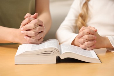 Photo of Girl and her godparent praying over Bible together at table indoors, closeup