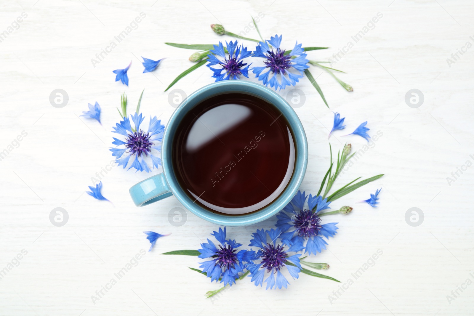 Photo of Cup of tea and cornflowers on white wooden table, flat lay