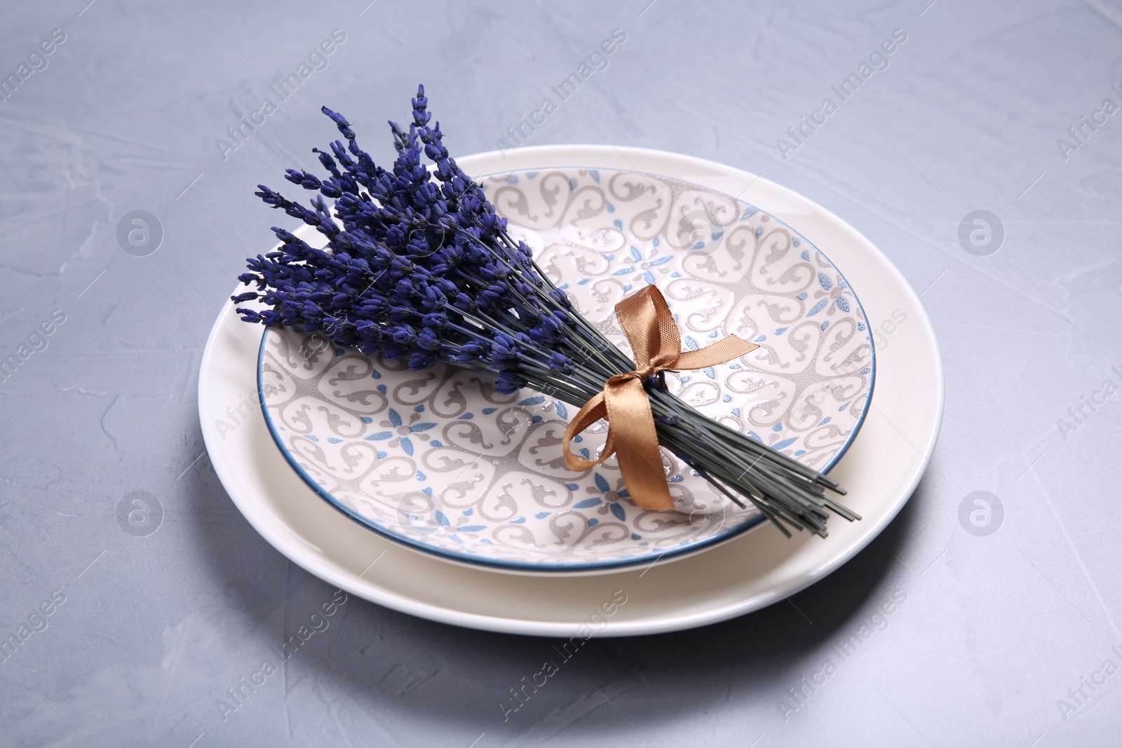 Photo of Bouquet of beautiful preserved lavender flowers and plates on light grey textured table