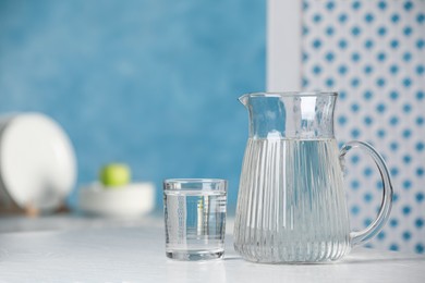 Jug and glass with water on white table indoors, space for text