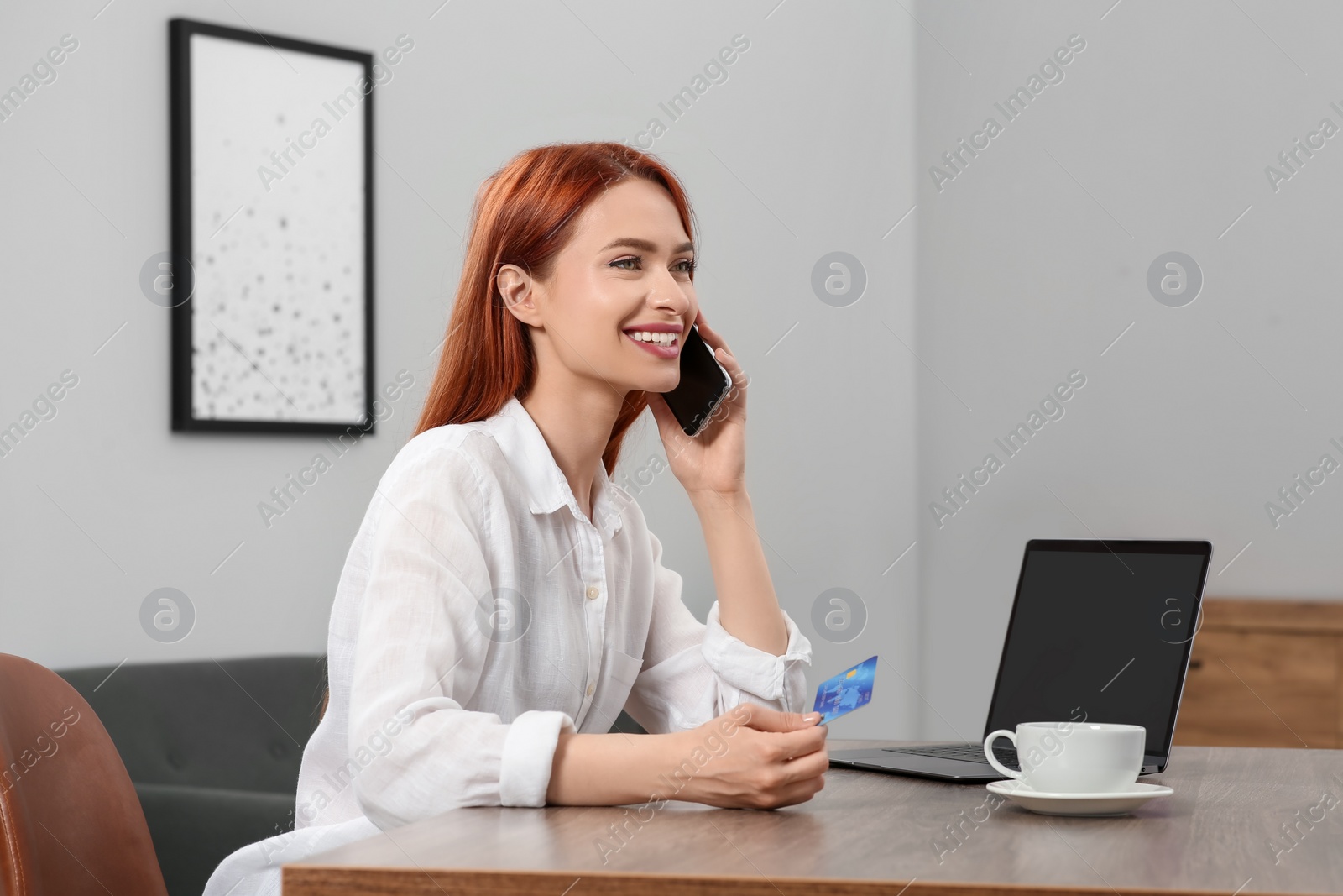 Photo of Happy woman with credit card using smartphone for online shopping at wooden table in room. Space for text