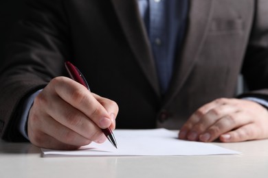 Man writing on sheet of paper with pen at white wooden table, closeup