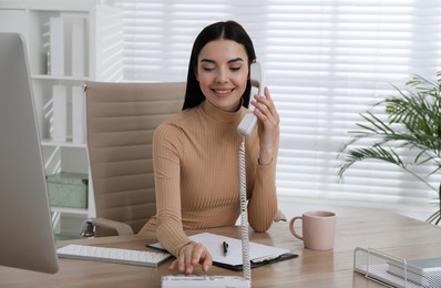 Photo of Secretary talking on phone at wooden table in office