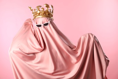 Glamorous ghost. Woman in sheet with sunglasses and crown on pink background