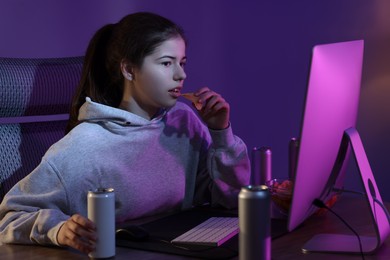 Photo of Girl with energy drink eating chips and playing computer game at home