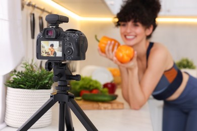 Photo of Food blogger explaining something while recording video in kitchen, focus on camera