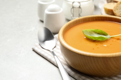 Photo of Tasty creamy pumpkin soup with basil in bowl on grey table. Space for text