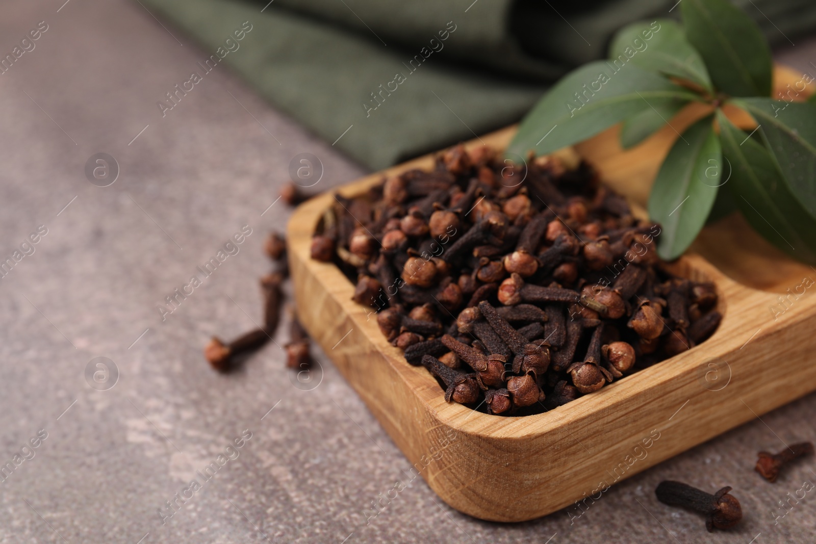 Photo of Wooden tray with aromatic cloves and green leaves on brown table, closeup. Space for text