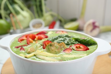 Photo of Saucepan with delicious green curry chicken soup on wooden board, closeup