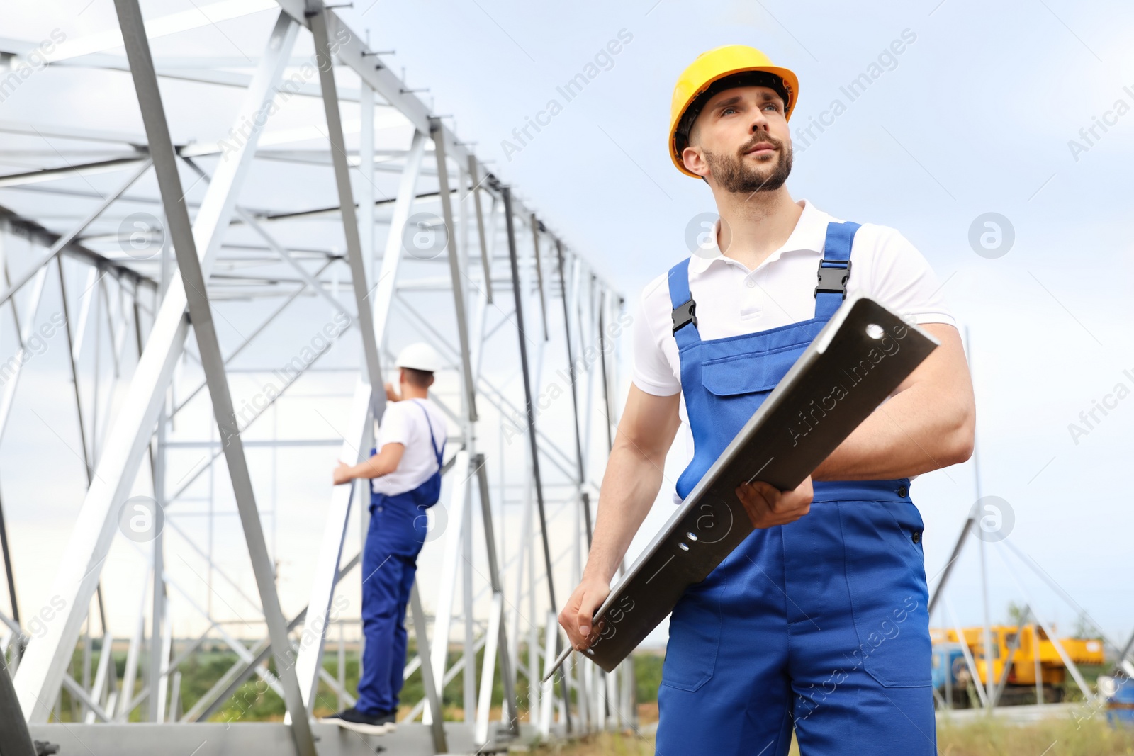 Photo of Workers building high voltage tower construction outdoors. Installation of electrical substation