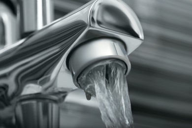 Photo of Water flowing from bath tap on blurred background, closeup