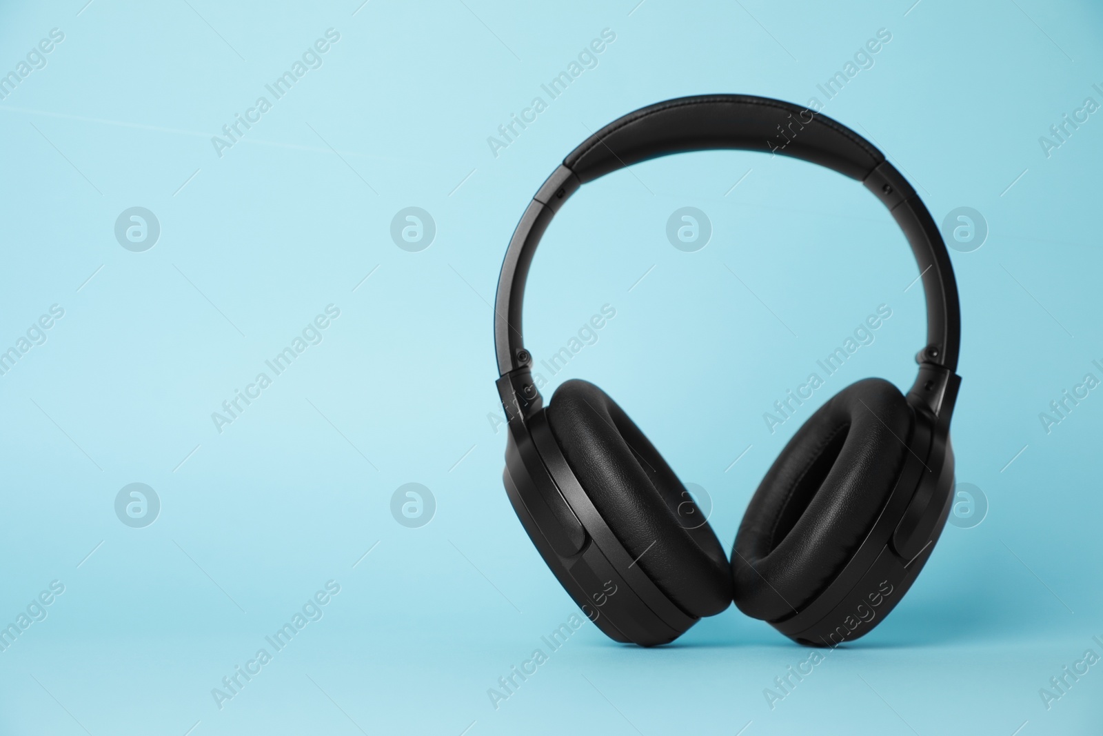 Photo of Modern wireless headphones on light blue background. Space for text