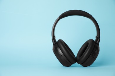 Photo of Modern wireless headphones on light blue background. Space for text