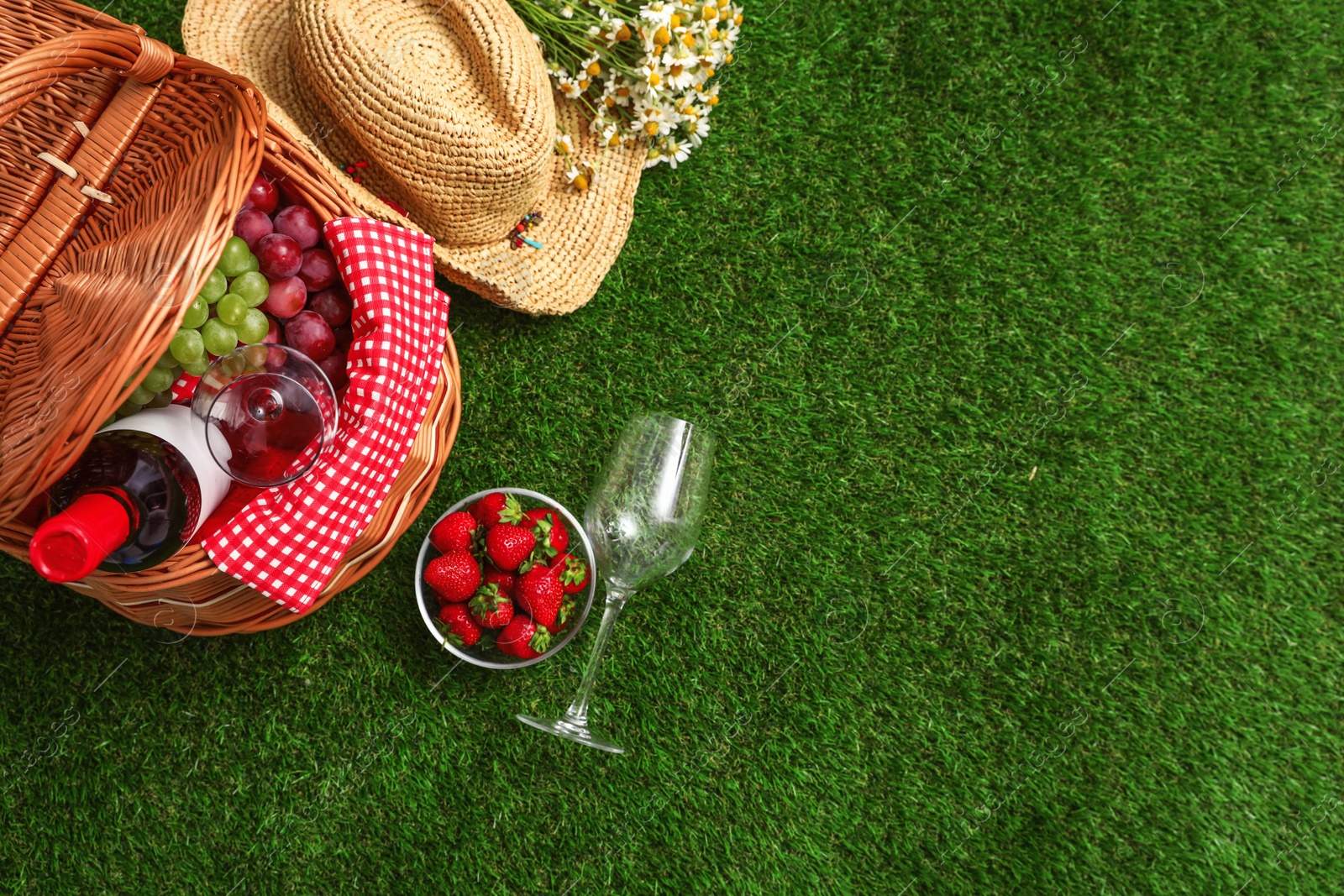 Photo of Flat lay composition with picnic basket, wine and fruits on grass, space for text