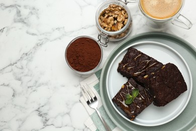 Delicious chocolate brownies with nuts, caramel sauce and coffee on white marble table, flat lay. Space for text