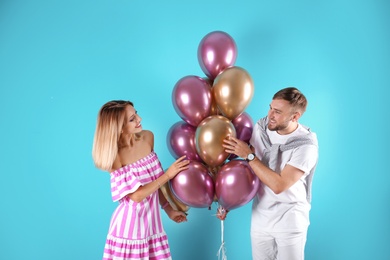 Young couple with air balloons on color background