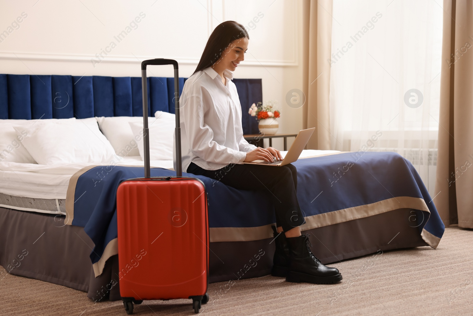 Photo of Beautiful young business woman working with laptop on bed in hotel room