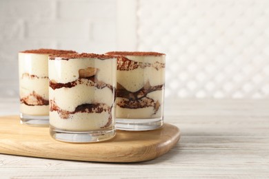 Photo of Delicious tiramisu in glasses on light wooden table. Space for text