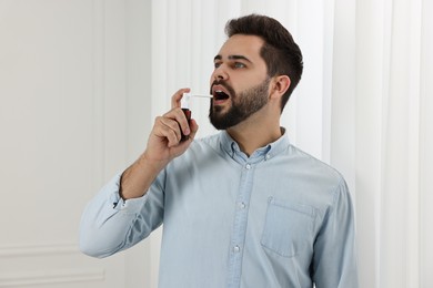 Young man using throat spray at home