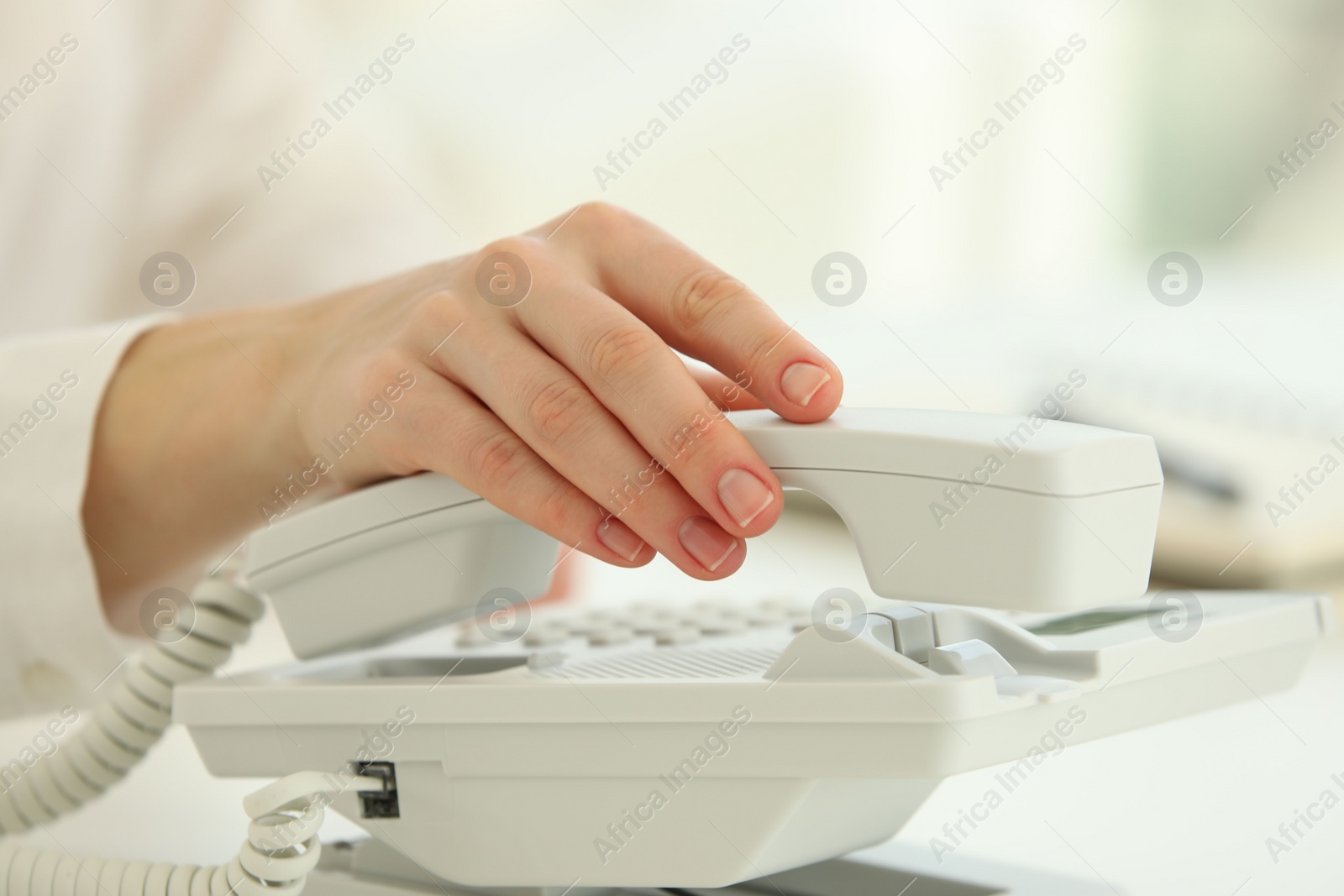 Photo of Assistant taking telephone handset at white table, closeup