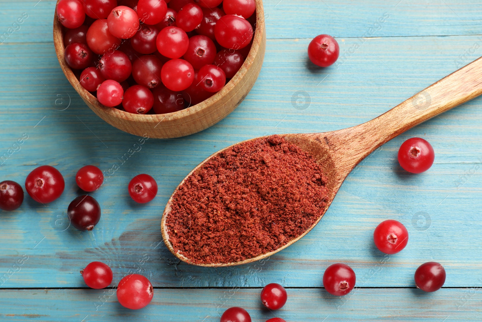 Photo of Spoon with cranberry powder and fresh berries on light blue wooden table, flat lay