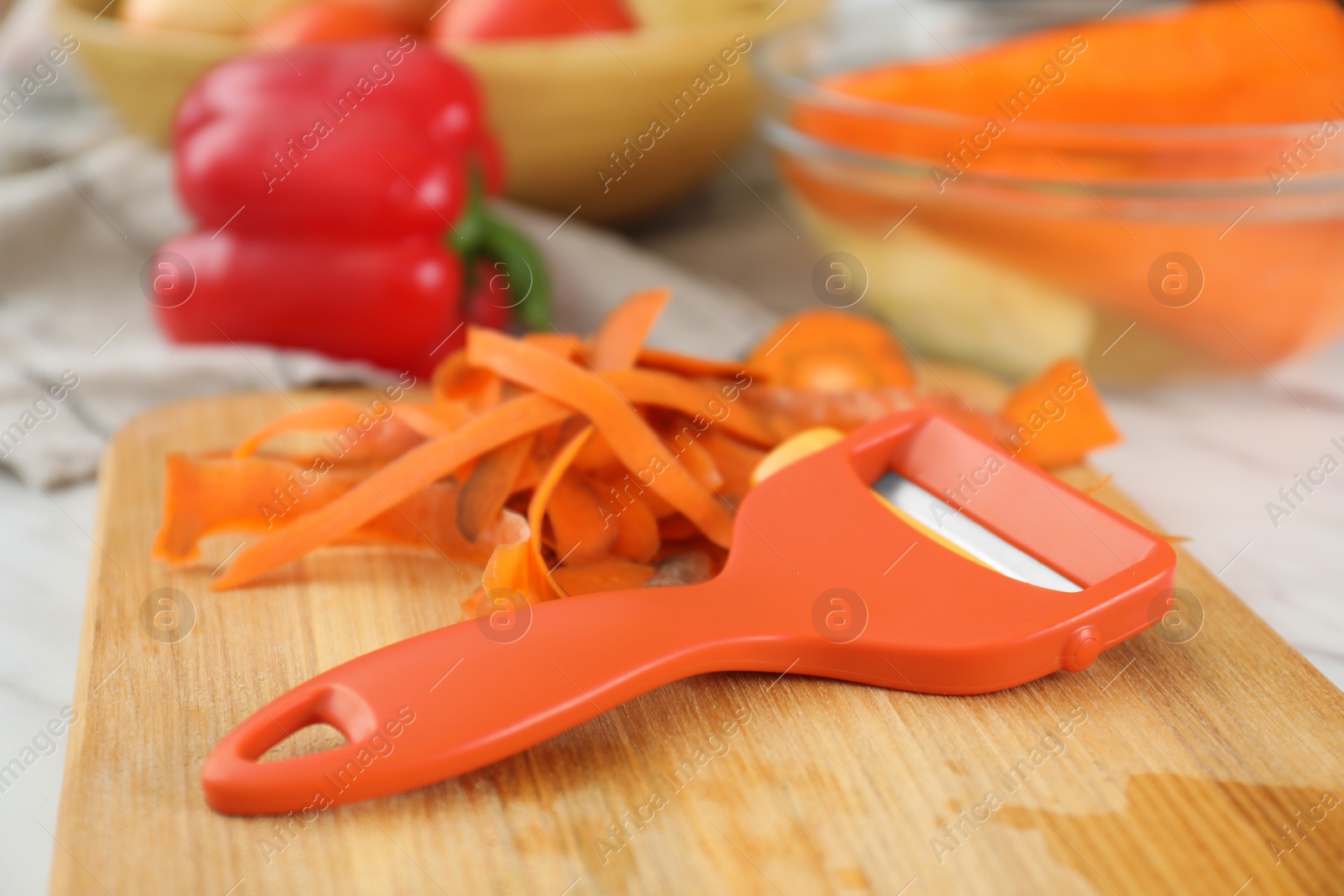 Photo of Wooden board with carrot peels and peeler on white table, closeup