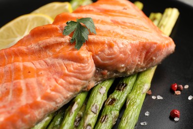 Tasty grilled salmon with asparagus and spices on plate, closeup