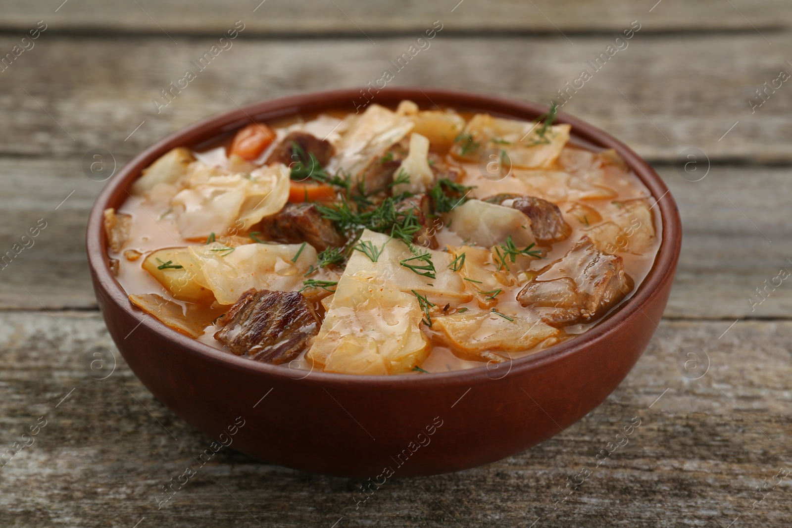 Photo of Tasty cabbage soup with meat, carrot and dill on wooden table, closeup