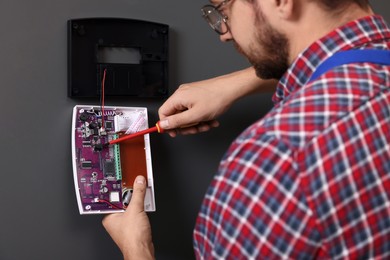 Photo of Technician installing home security alarm system on gray wall indoors, closeup