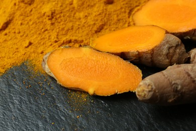 Turmeric powder and cut roots on black textured table, closeup