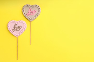 Photo of Chocolate heart shaped lollipops with word Love on yellow background, flat lay. Space for text