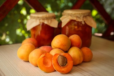 Photo of Delicious ripe apricots with jars of homemade jam on wooden table outdoors