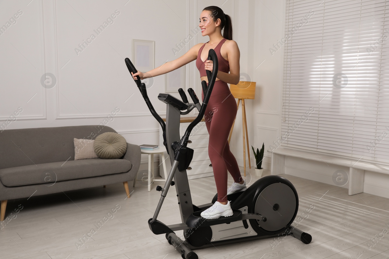 Photo of Happy young woman training on elliptical machine at home