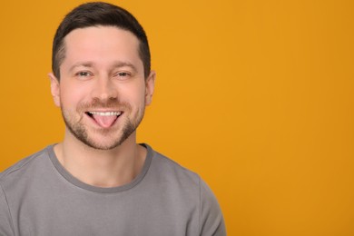Photo of Happy man showing his tongue on orange background. Space for text