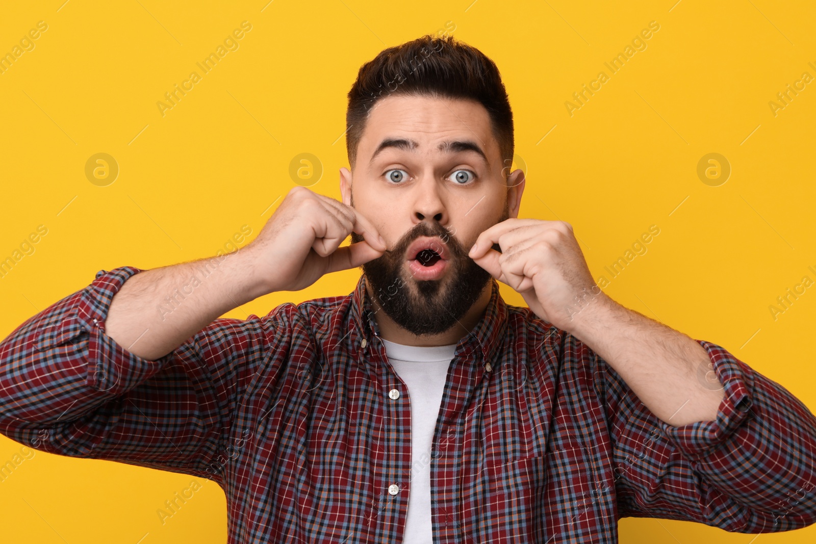 Photo of Surprised young man touching mustache on yellow background