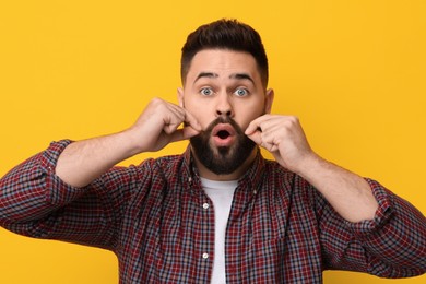 Surprised young man touching mustache on yellow background