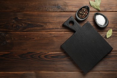 Photo of Black cutting board, salt, pepper and bay leaves on wooden table, flat lay. Space for text