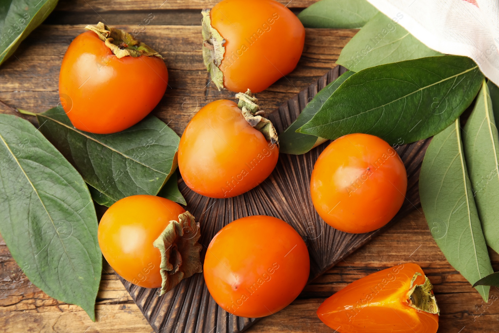 Photo of Delicious fresh persimmons and green leaves on wooden table, flat lay