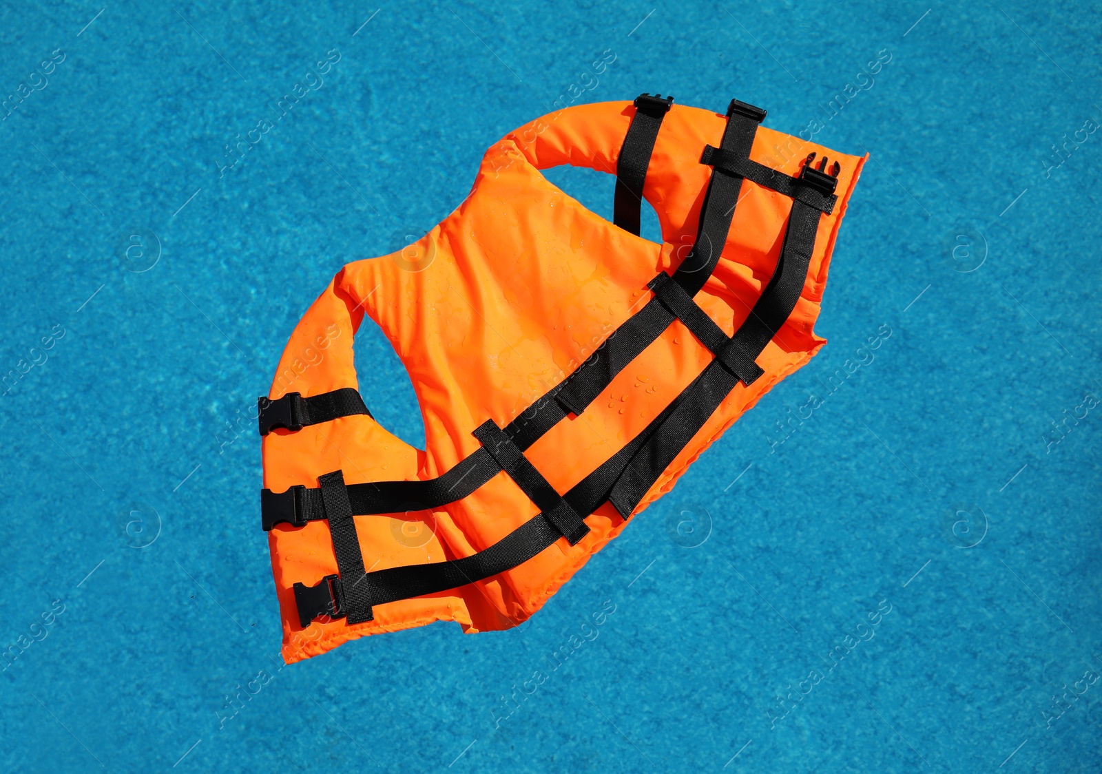 Photo of Bright orange life jacket floating in swimming pool, top view