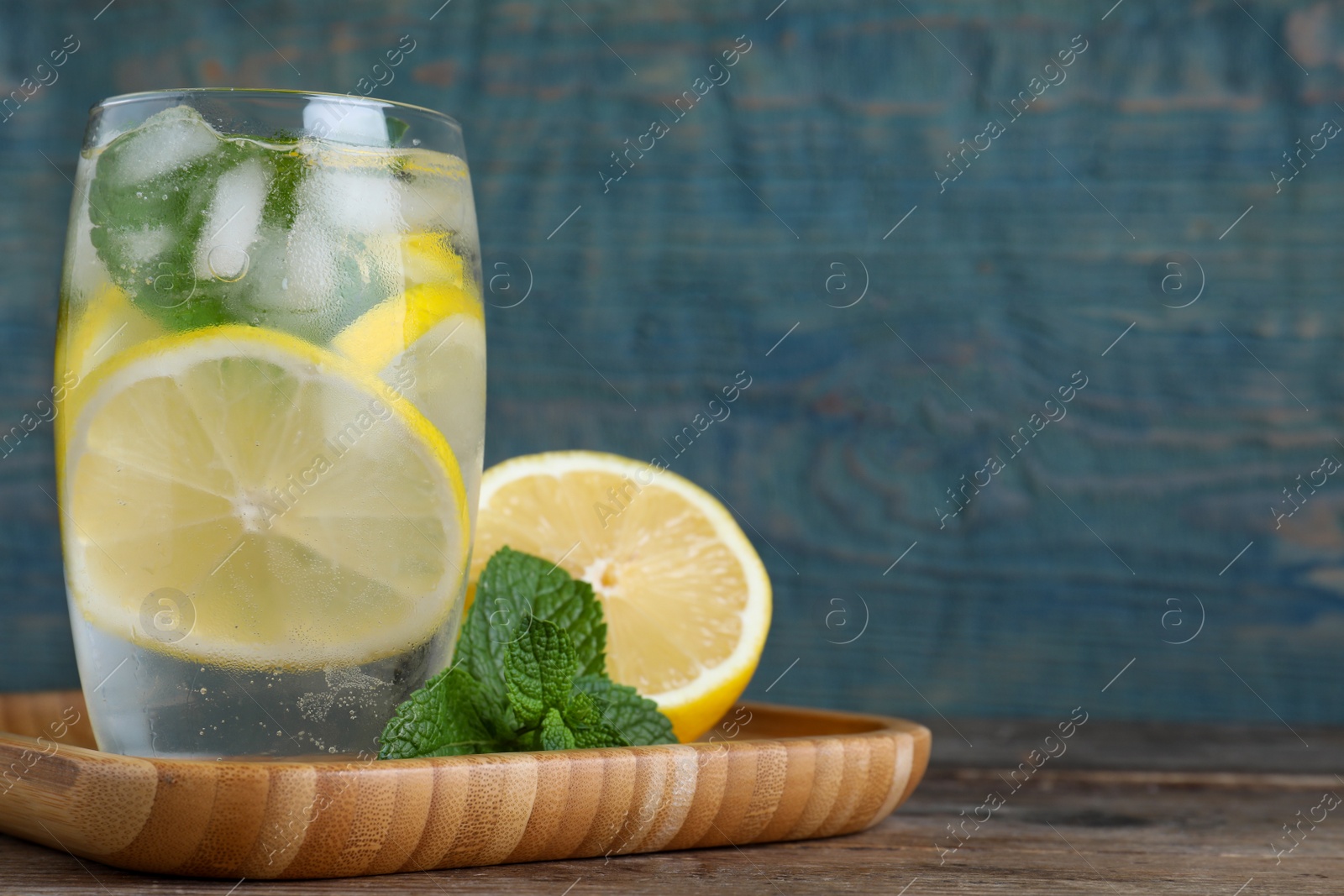 Photo of Delicious lemonade made with soda water and fresh ingredients on wooden table against light blue background. Space for text