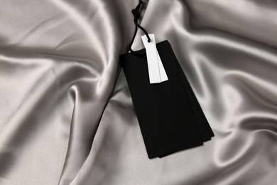 Photo of Blank black tags on silver silky fabric. Space for text