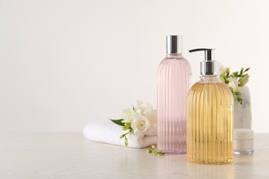 Liquid soap in stylish dispenser, bottle of shower gel, cream, towel and flowers on white table, space for text